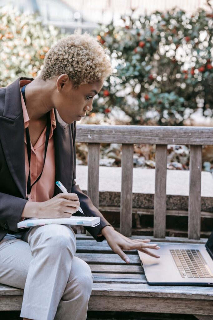 Concentrated ethnic student taking notes and using laptop